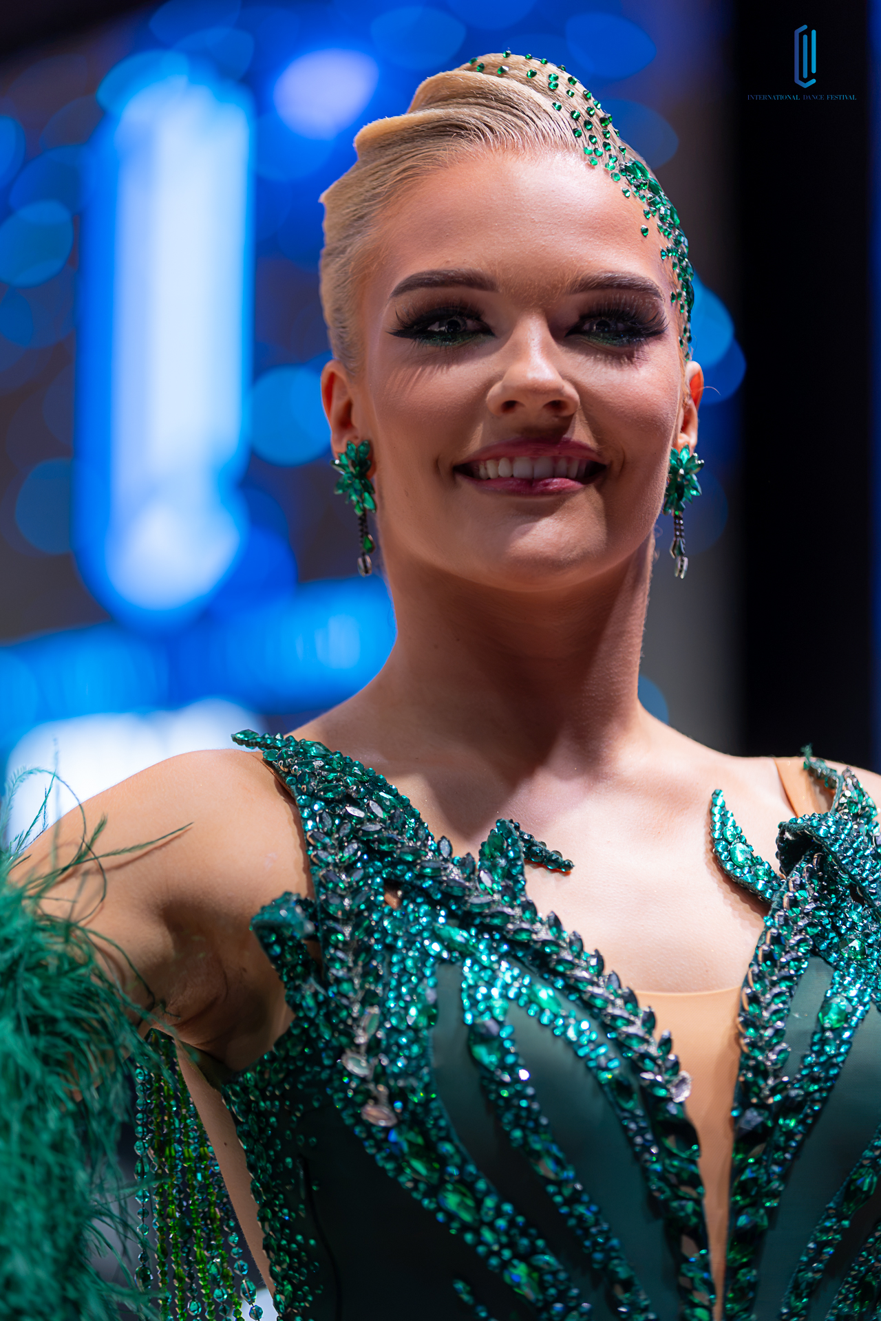 A ballroom couple in a close embrace, framed by white feathers and blue lights